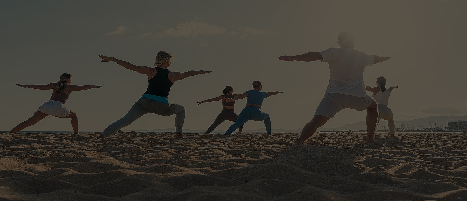 Group practicing yoga on the beach at sunset.