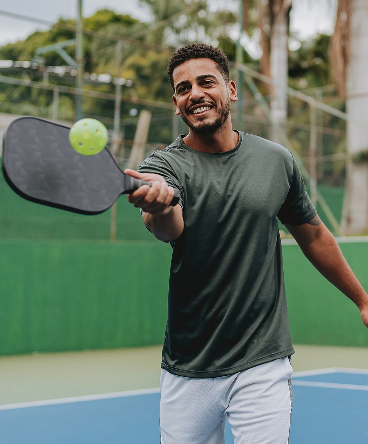 Smiling man playing pickleball in court.